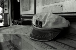 A black and white image of a captain's hat on a ship's desk, capturing a vintage maritime ambiance.