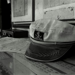 A black and white image of a captain's hat on a ship's desk, capturing a vintage maritime ambiance.